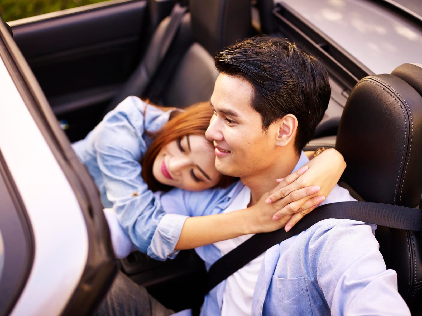 柔らかな日差しの中、車の座席から振り返るグレーのセーターを着た女性。